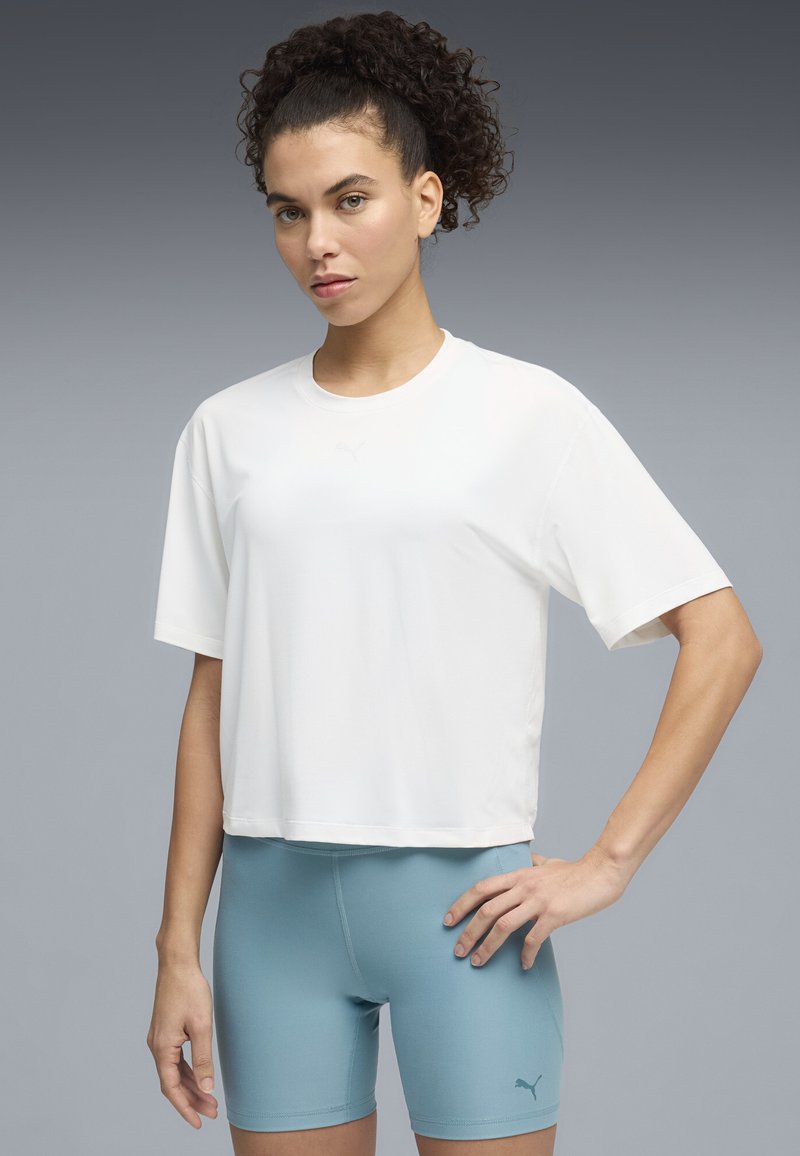 Λευκό κοντομάνικο cropped t-shirt με στρογγυλή λαιμόκοψη, με ένα διακριτικό λογότυπο στο μπροστινό μέρος. Συνδυάζεται με ανοιχτό μπλε εφαρμοστά σορτς.