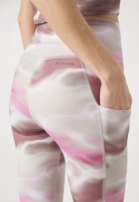 Leggings med ett vågigt mönster i rosa och beige, tillverkade av ett glatt material, med en sidoficka och Columbia-logotypen nära midjan.