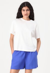 Hvit bomull t-skjorte med korte ermer, rund utringning, løs passform, kombinert med blå bomullsshorts med elastisk midjebånd og sidelommer.