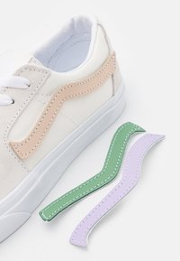 Baskets en toile blanche avec des accents en daim beige et des lacets blancs. Comprend des éléments décoratifs amovibles en cuir vert et lavande.