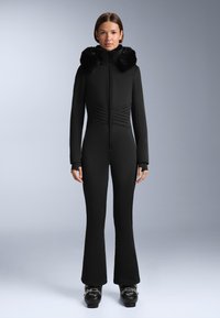 Czarny kombinezon narciarski o dopasowanym kroju, z futrzanym kołnierzem, długimi rękawami i rozszerzanymi spodniami. Strukturalna tkanina z ukośnymi szwami.