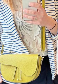Kleine gele schoudertas van gestructureerd leer met een gebogen klep en twee banden. Draag je over een licht, bloemenpatroon top.