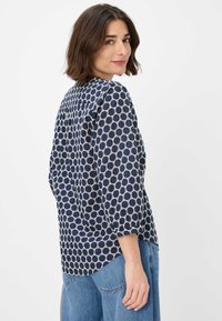 Navyblaue Bluse mit ovalem Druckmuster, Dreiviertelärmeln und einem lässigen Schnitt mit abgerundetem Saum und Schlitzdetails im Rücken.