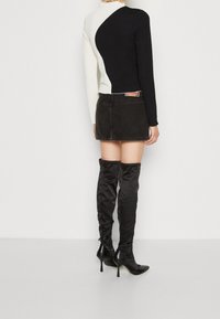 Schwarzes und weißes, strukturiertes Oberteil mit einem einzigartigen asymmetrischen Design, kombiniert mit einem schwarzen Denim-Rock und schwarzen, knöchelhohen Stilettos.