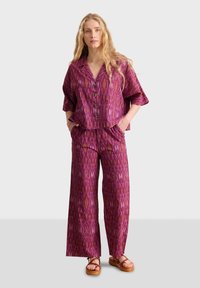 Conjunto de dos piezas que incluye una blusa de manga corta y botones y pantalones de pierna ancha en un vibrante magenta con un patrón geométrico.