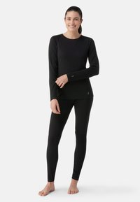Svart långärmad topp och leggingsset gjort av slät tyg. Har en enkel design med subtila loggoförstärkningar på ärmslut och nederkant.