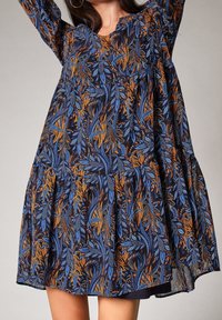 Robe fleurie en tissu sombre, présentant des motifs de feuilles bleues et orange, des manches longues, un col rond et une jupe à volants.