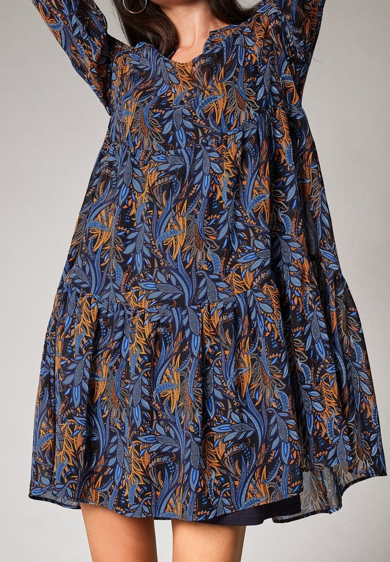 Robe fleurie en tissu sombre, présentant des motifs de feuilles bleues et orange, des manches longues, un col rond et une jupe à volants.
