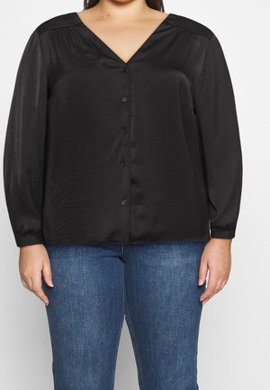 Woman wearing a black long-sleeve button-up blouse with a V-neck and blue jeans, shown from shoulders to hips against a plain background.