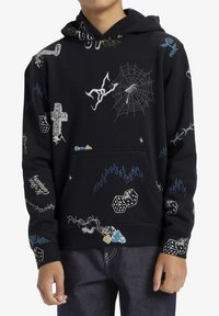 Svart hoodie med varierande grafiska tryck, inklusive kors, spindelnät och tärningar. Har en känguruficka och ribbade ärmslut.