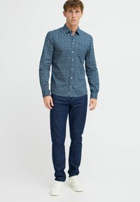 Camicetta a manica lunga blu con motivo a foglie, colletto alla francese e polsini, abbinata a jeans scuri e sneakers bianche.