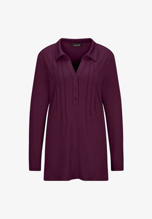 Langemouwen, pruimenblouse met een knoopsluiting bij de kraag en een geplooide voorkant, gedragen met opgerolde blauwe jeans en witte sneakers.