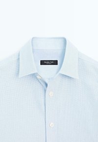 Jasnoniebieska koszula z guzikami, wykonana z fakturowanej tkaniny. Ma kołnierz rozłożony i cztery białe guziki na plisie z czarną metką.