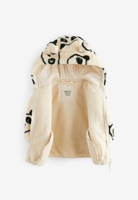Veste polaire couleur crème avec imprimés abstraits de visages noirs, ouverture devant et capuche attachée avec petites oreilles en tissu.