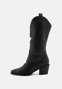 Czarne skórzane kowbojskie buty z ostrym noskiem, sięgające do połowy łydki, z srebrnymi akcentami w kształcie gwiazd oraz grubym obcasem. Widoczne są detale szwów.