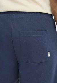 Pantalons de jogging bleu marine en matériau doux avec une finition texturée, dotés d'une poche arrière rectangulaire et d'une petite étiquette de marque sur le côté.