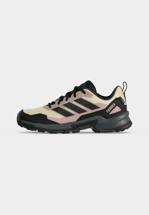 Beige en zwarte Adidas Terrex wandelschoen met roze accenten, zwarte zool en zwarte veters, zijaanzicht op een witte achtergrond.