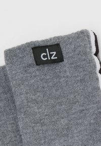 Šedá látka s jemnou pletenou texturou. Černá etiketa s bílými písmeny "clz" je viditelná. Na jedné straně zvýrazněná bílým okrajem.