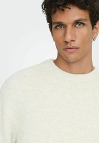 Pull en tricot blanc avec un col rond, doté d'un tissu doux et texturé. Design simple et coupe décontractée, mettant en valeur un style épuré et minimaliste.