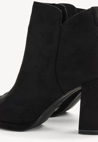 Black suede ankle boots with a square toe, high block heel, and minimal stitching detail on the sides. The heel is slightly textured.