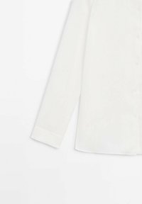 Chemise blanche à manches longues avec col pointu, tissu net et texture lisse ; présente des détails de boutons à l'avant.