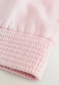 Tela rosa con un puño texturizado y fruncido. El material parece suave y elástico, con pliegues espaciados de manera uniforme a lo largo de la banda.