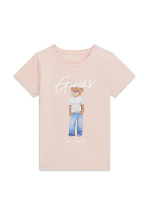 T-shirt rose clair avec un motif d'un ours portant un t-shirt blanc Guess et un jean bleu, avec le texte "Guess" au-dessus.