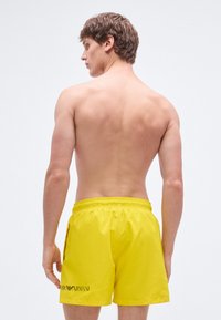 Dzelteni peldēšanas šorti no viegla materiāla ar elastīgu jostu un sānu kabatām. Melns logotips uzdrukāts apakšējā kreisajā pusē.