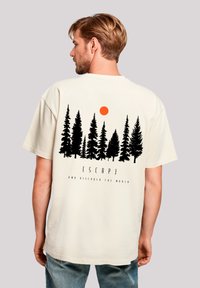 Cream t-shirt featuring a black forest silhouette and an orange sun, with text reading "ESCAPE AND DISCOVER THE WORLD" below the design.