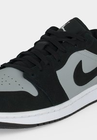 Μαύρο και γκρι αθλητικό παπούτσι Nike με μαύρα κορδόνια, λευκή ενδιάμεση σόλα, διάτρητη περιοχή στα δάχτυλα και μαύρο λογότυπο Nike στο πλάι.