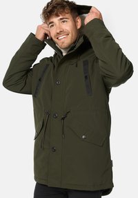 Olive green parka jacket with black accent stripes, large front buttons, drawstrings at the waist and hood, and a front flap pocket.