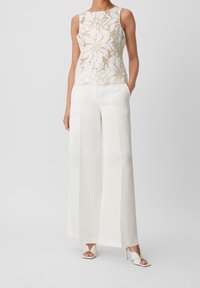 Kränkelös topp i kräm med blommönster, i kombination med högmidjade, vida vita byxor och sandaler med klack och remmar i vitt.