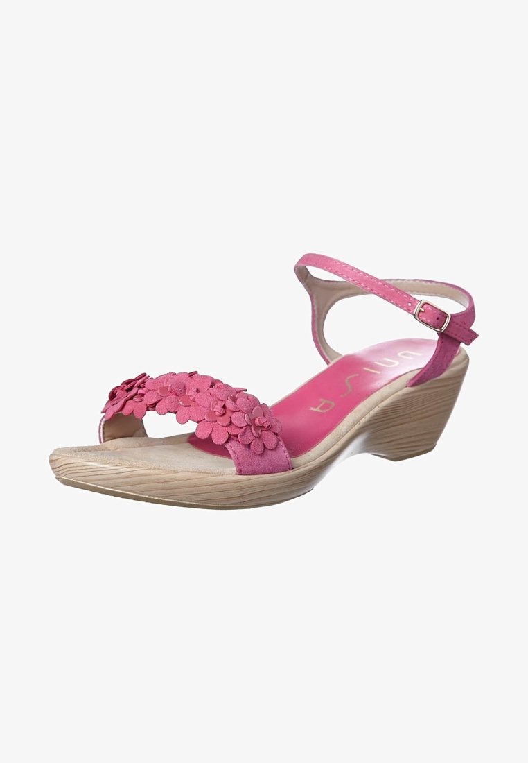 Pink wedge sandal with floral embellishments on the strap, curved design, and a textured sole. Adjustable ankle strap for fit.