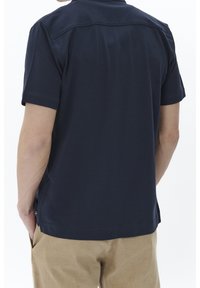 Marinblå kortärmad t-shirt med en slät textur, som har en sömdetalj över den övre delen av ryggen och sidoklaffar vid nederkanten.