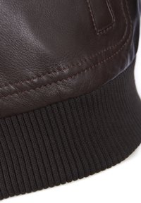 Brun læderjakke detaljer med struktureret læder, mørk ribstrikket manchet og kontrasterende syninger langs sømmen.