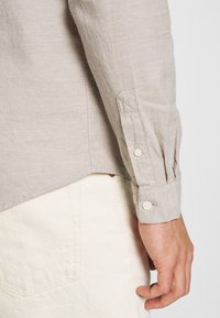 Grijze linnen overhemd met lange mouwen en knoopmanchetten, voorzien van een iets afgeronde zoom en subtiele textuur, gecombineerd met crèmekleurige broek.