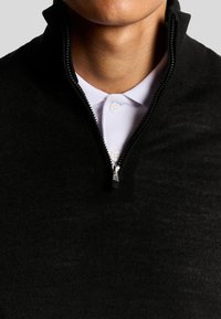 Pullover nero con zip e colletto alto, realizzato in tessuto testurizzato. Indossato sopra una polo chiara con bottoni visibili.