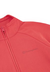 Rode sportieve rits-top met hoge kraag, voorzien van een subtiel logo en een gladde, textuurrijke stof. Ritsluiting met een slank, modern ontwerp.