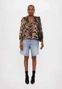 Black and gold patterned blouse, relaxed fit; light blue denim shorts with frayed hem; black ankle socks; pointed black heels; black bag.