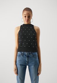 Svart ermeløs topp med høy hals, prydet med hvite prikker. Kombinert med lyseblå høyhvit jeans.