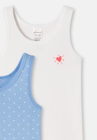 Dvě bezrukávové dětské trička, jedno bílé s malým červeným srdíčkem, druhé modré s bílými puntíky, obě z organické bavlny, velikost 3-4 roky.
