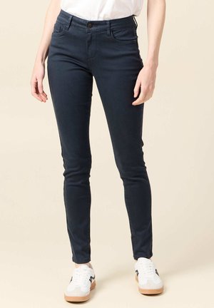 Jeans skinny blu navy con cinque tasche, chiusura frontale con bottone e un tessuto liscio e elastico. Abbinati a sneakers bianche.