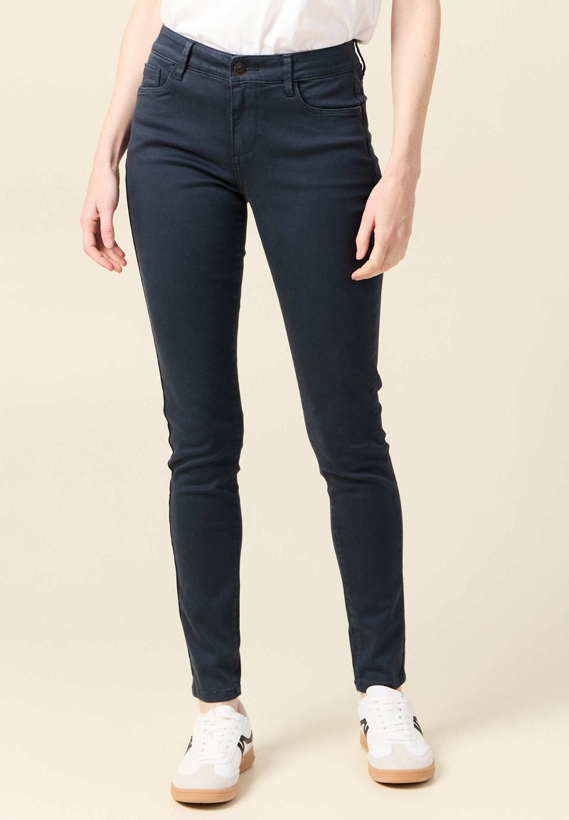 Jeans skinny azul marino con cinco bolsillos, cierre frontal con botón y una tela suave y elástica. Combinados con zapatillas blancas.