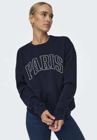 Jūras spēku džemperis ar baltu tekstu "PARIS", brīvs piegriezums, apaļa kakla izgriezums, ribotām piedurknēm un jostasvietai. Mīksta auduma tekstūra un vienkārša dizaina.