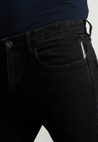 Mustat farkut, joissa on slim fit -leikkaus, metallinen nappikiinnitys, etutaskut ja huomaamaton hopeinen yksityiskohta sivulla.