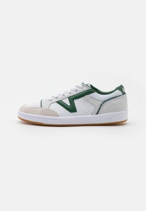 White sneaker with green accents, suede toe cap, lace closure, and perforated detailing. Gum rubber sole for traction.