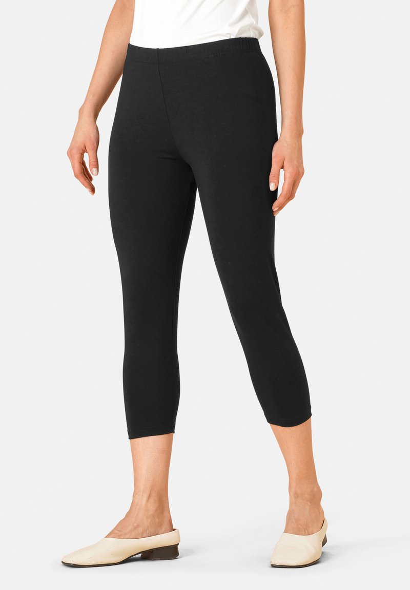 Zwarte capri leggings gemaakt van zachte rekbare stof met een elastische tailleband, een getailleerd ontwerp en een cropped lengte, gecombineerd met lichte flatjes.