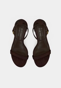 Καφέ σανδάλια από vegan δέρμα με επίπεδη σόλα, λουράκι στον αστράγαλο και δύο φαρδιές λουρίδες στο πέλμα. Υφή με λεπτομέρεια λογότυπου στην εσωτερική σόλα.