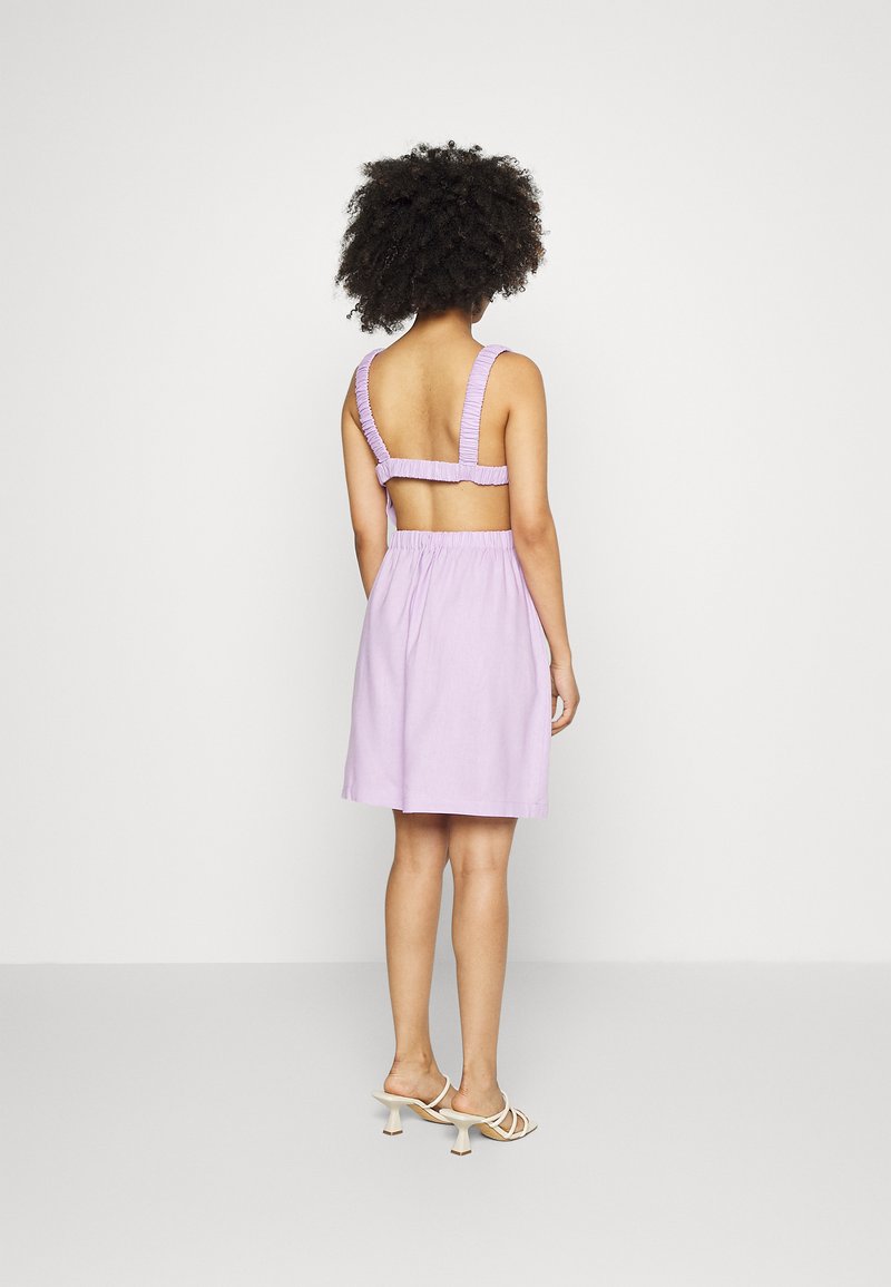 Vestido lilás com um corpete ajustado, alças elásticas e uma saia relaxada. Apresenta um recorte nas costas e detalhes texturizados nas alças.