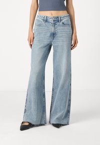 Ανοιχτό μπλε τζιν παντελόνι σε φαρδύ στιλ, φτιαγμένο από τζιν ύφασμα, με ψηλή μέση, μπροστινές τσέπες και ξεφτισμένο στρίφωμα. Φοριέται με μαύρες μυτερές γόβες.